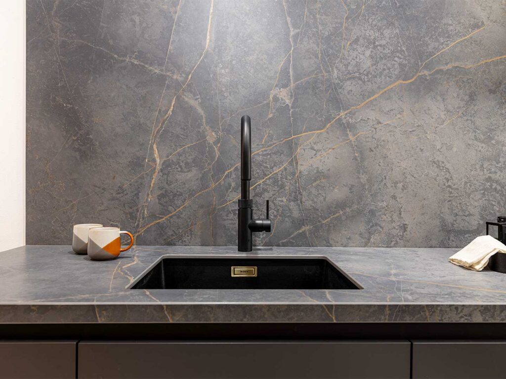 A black ceramic kitchen countertop with inset sink and matching splashback